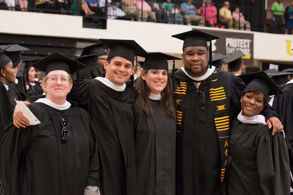 Diverse group of UMBC students in graduation attire posing at commencement