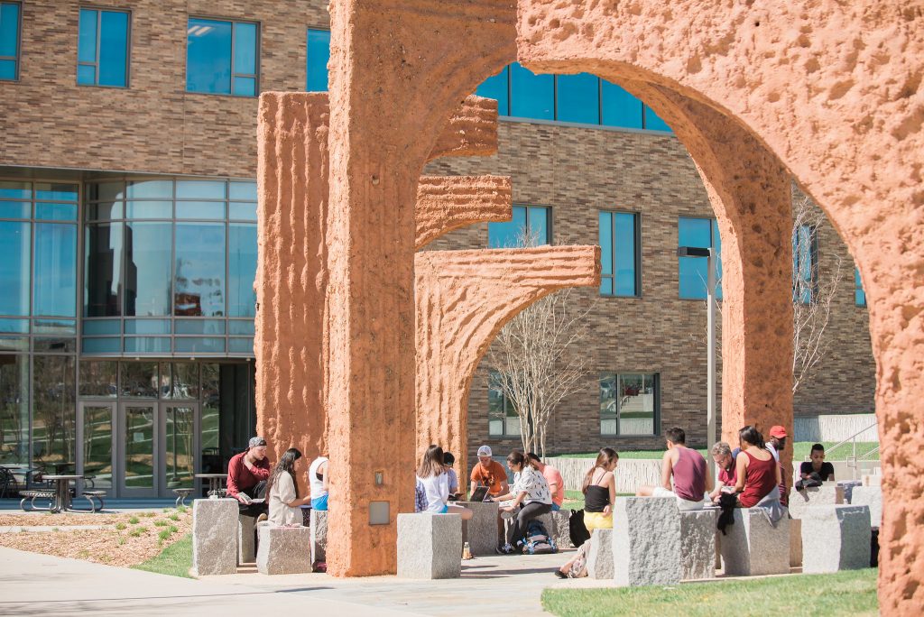 Groups of students sitting under the archway sculpture on campus