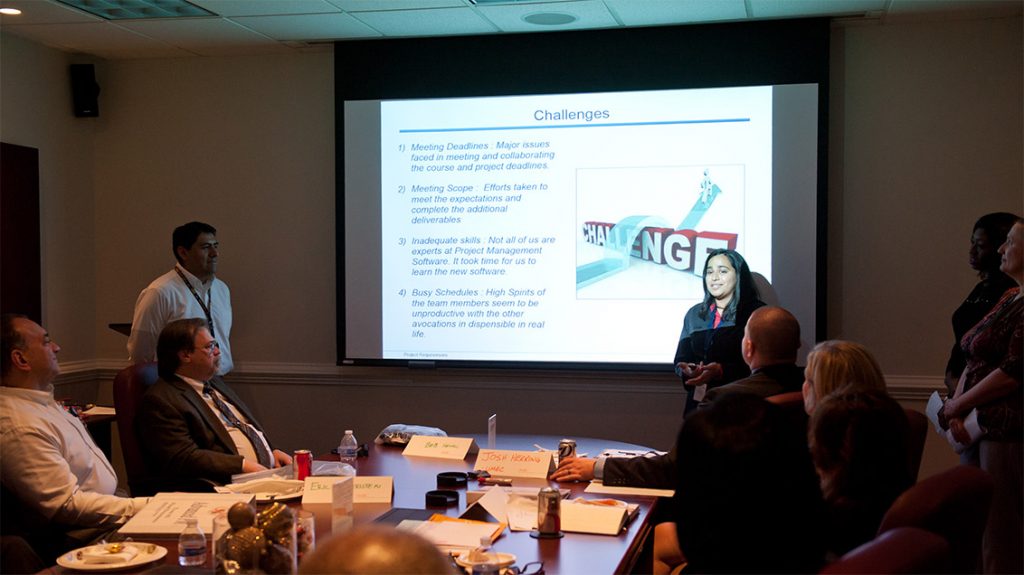Two students presenting to a group of professionals in a conference room